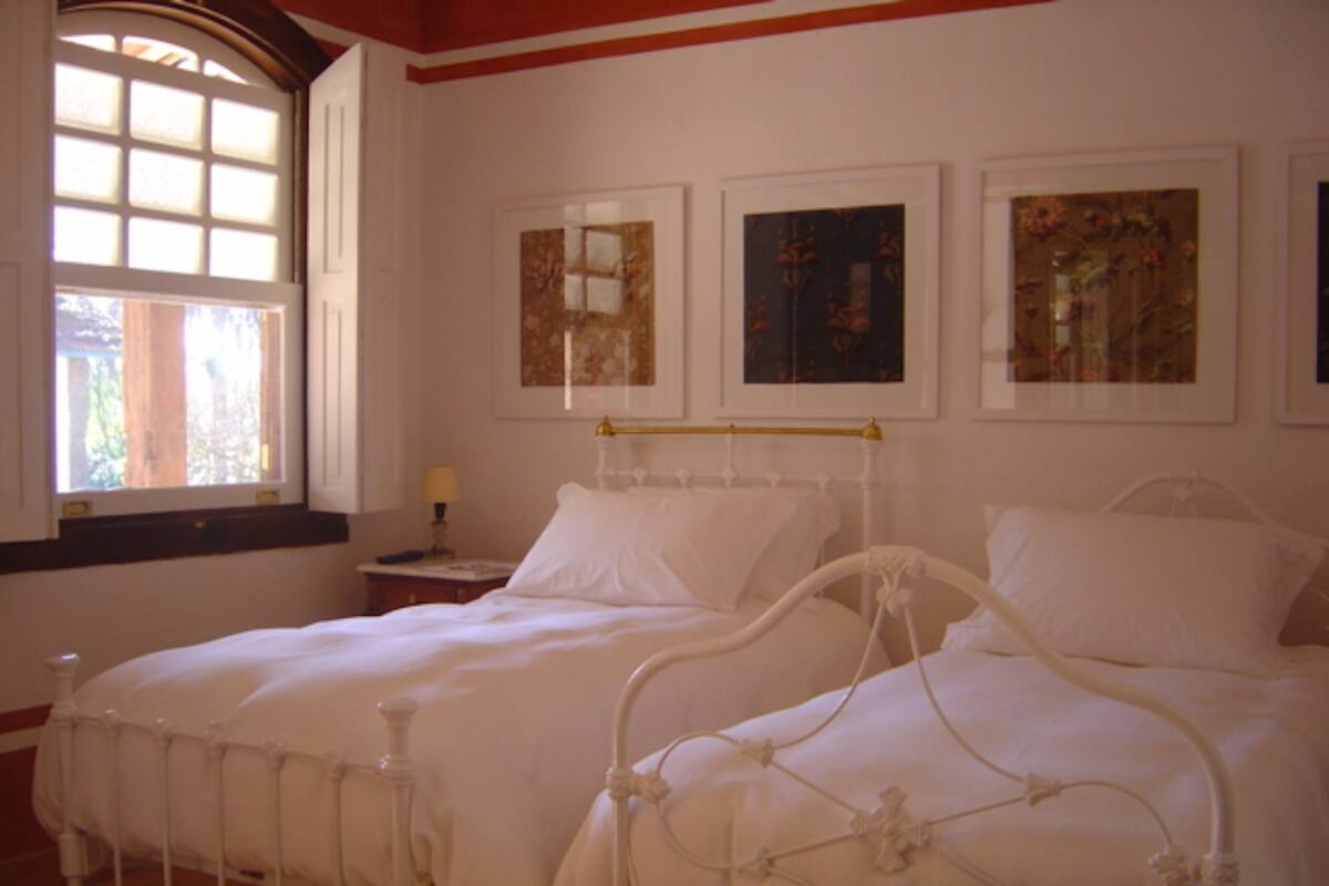 A bedroom with two beds, a window, and wall-mounted artwork.