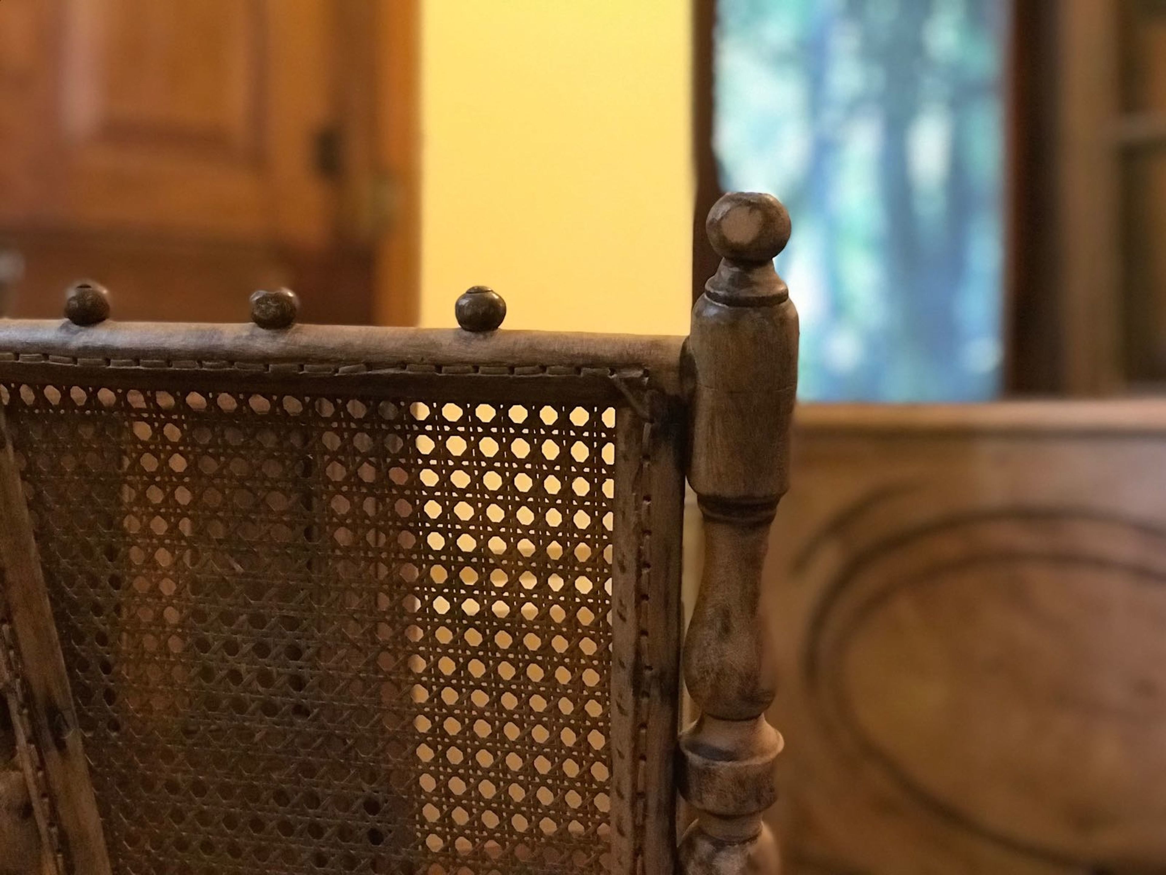 Primer plano de una silla de madera con respaldo trenzado y reposabrazos tallados.