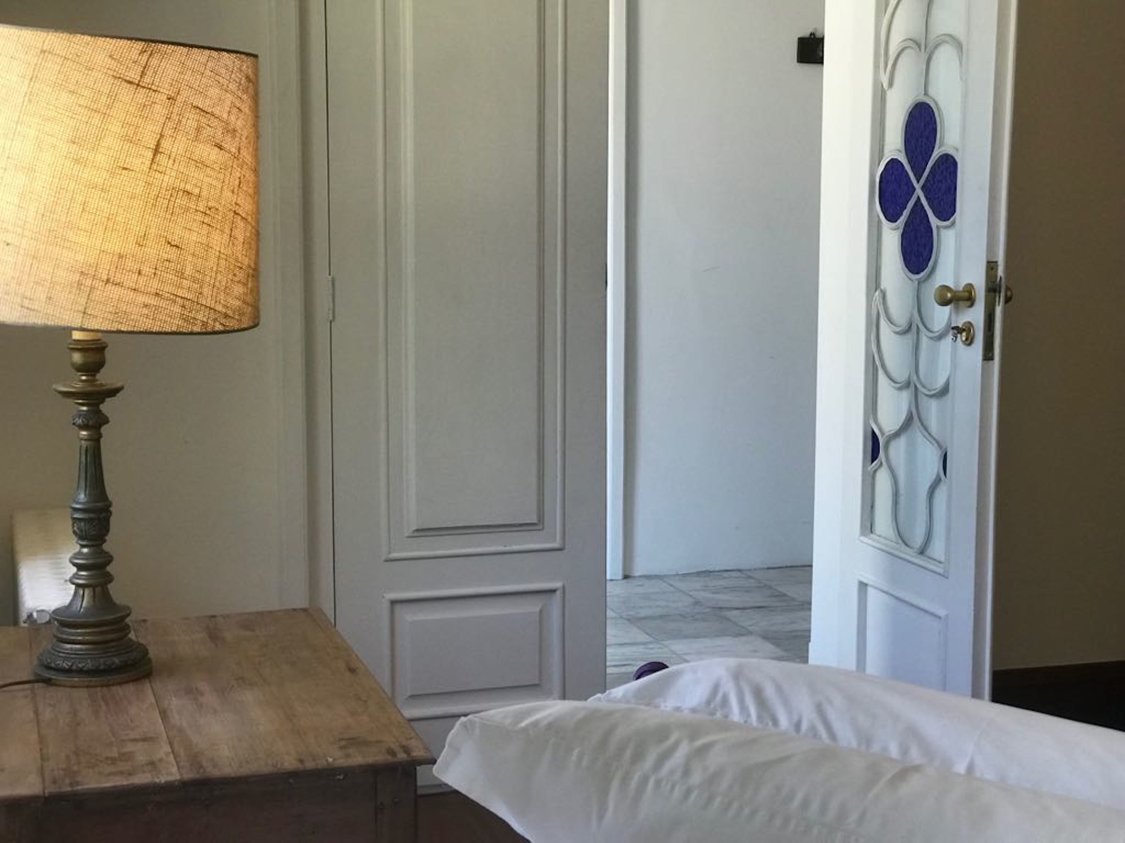 Ein Zimmer mit Nachttisch aus Holz, einer Lampe, einem Bett und einer Tür mit dekorativer Gestaltung.