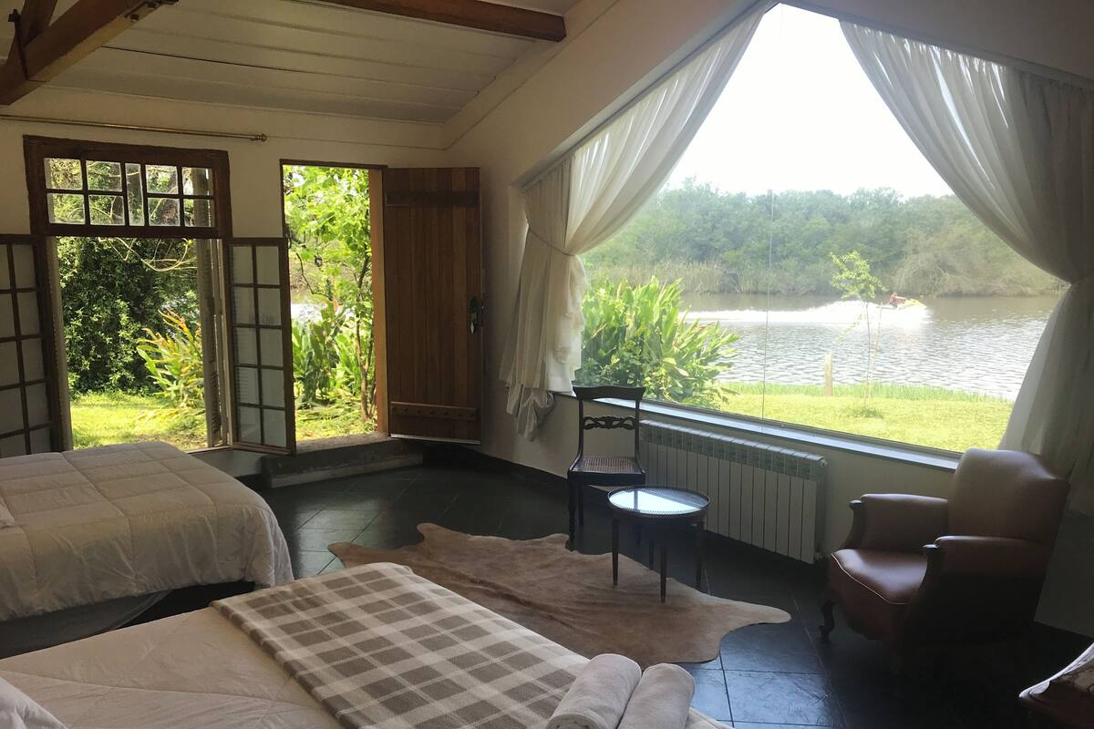 A room with two beds, a chair, a small table, and a view of a lake.
