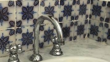 Un baño con un lavamanos blanco y dos grifos cromados. La pared detrás del lavamanos tiene azulejos blancos y azules con motivos florales.