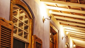 A corridor with wooden benches and arched windows, leading to a room with a red curtain. - Charqueada Santa Rita Pousada de Charme (Pelotas)