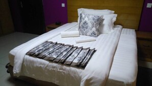 Una cama bien hecha con sábanas blancas, un plaid estampado y cojines decorativos.