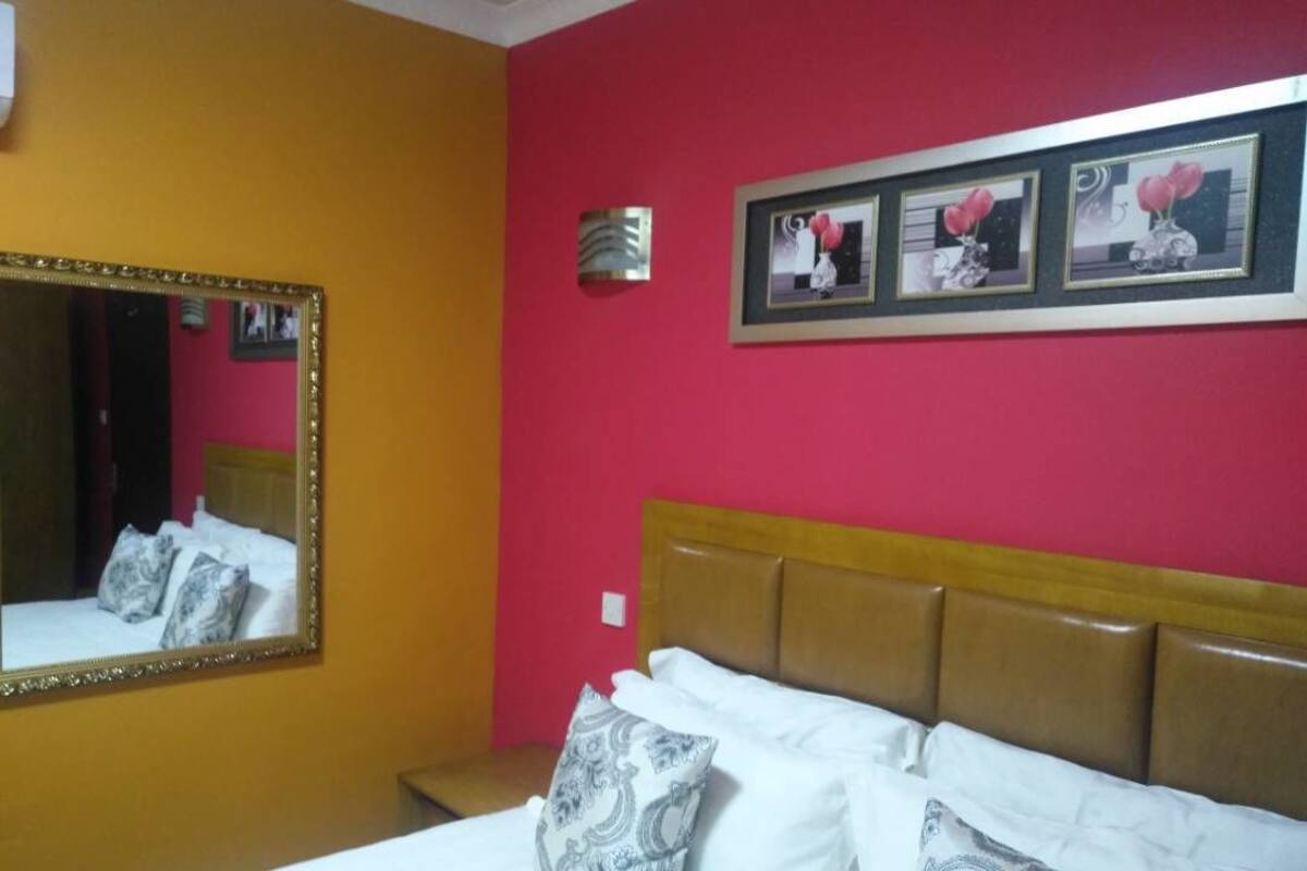 A hotel room with a bed, a large mirror, and three framed pictures on the wall.