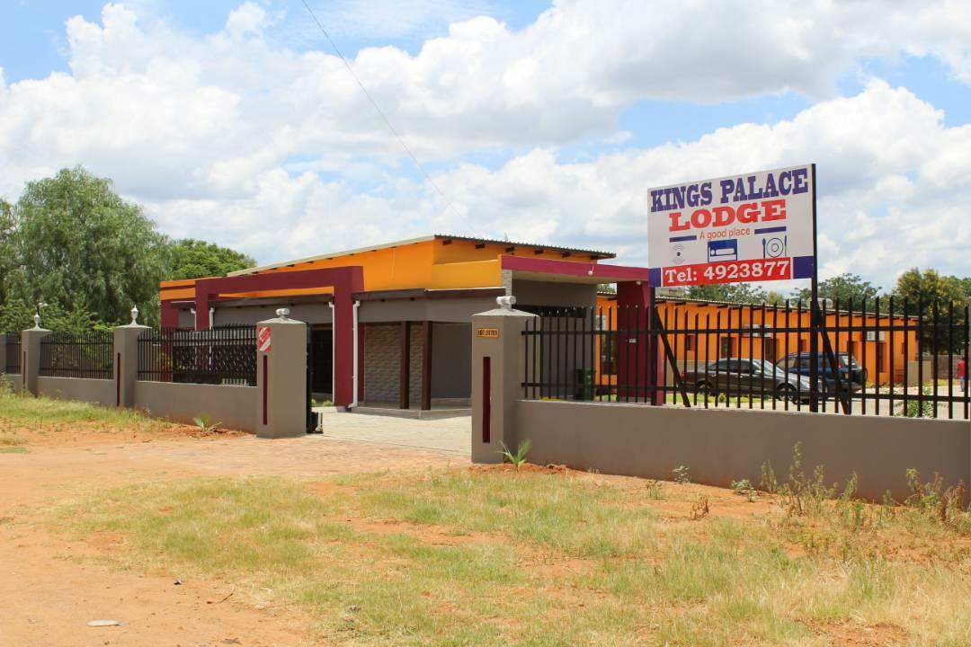Una residencia Kings Palace Lodge con entrada cercada, un cartel y un coche estacionado.