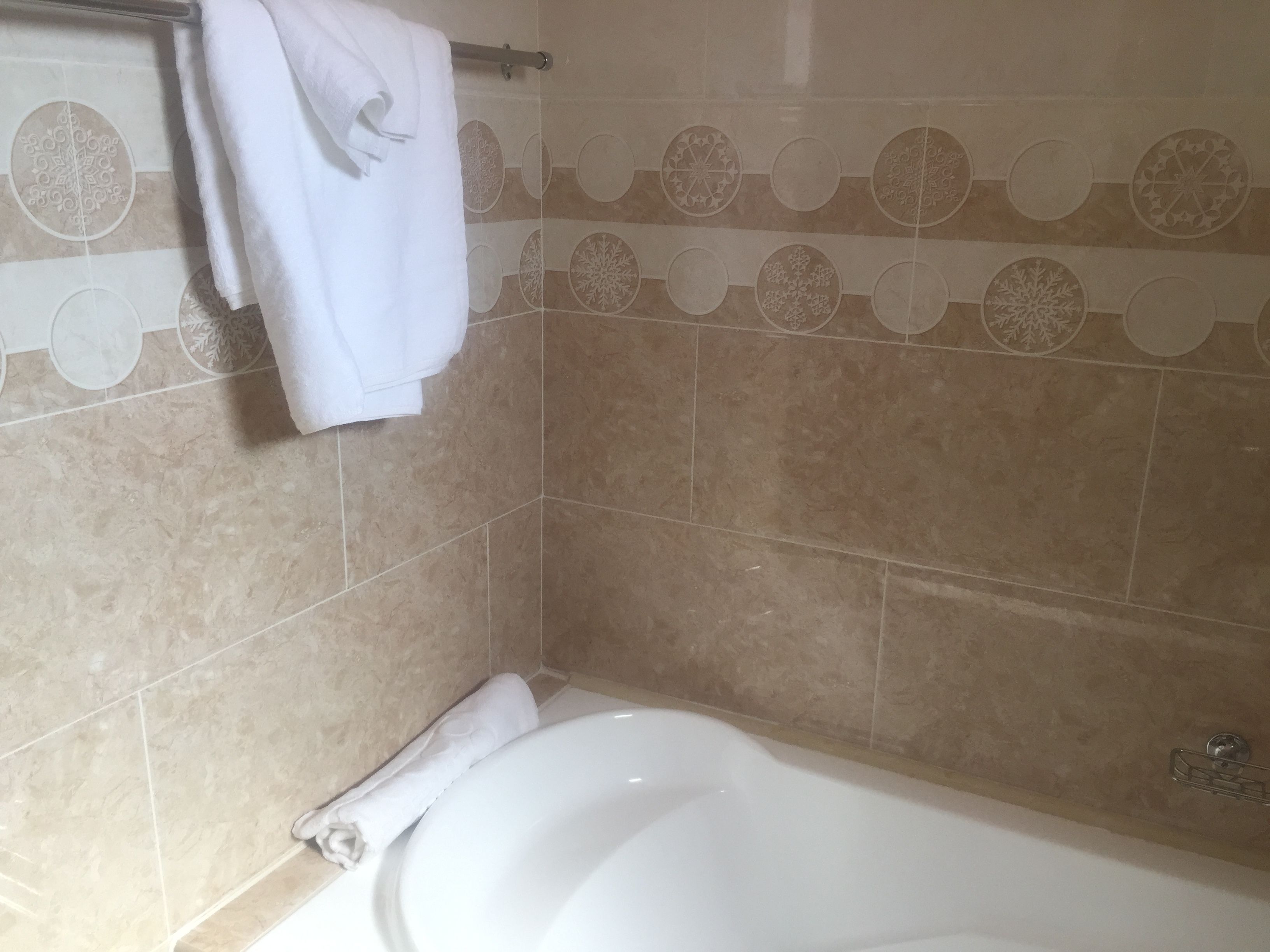 A bathroom with a bathtub, beige patterned tiles, and a towel rack.