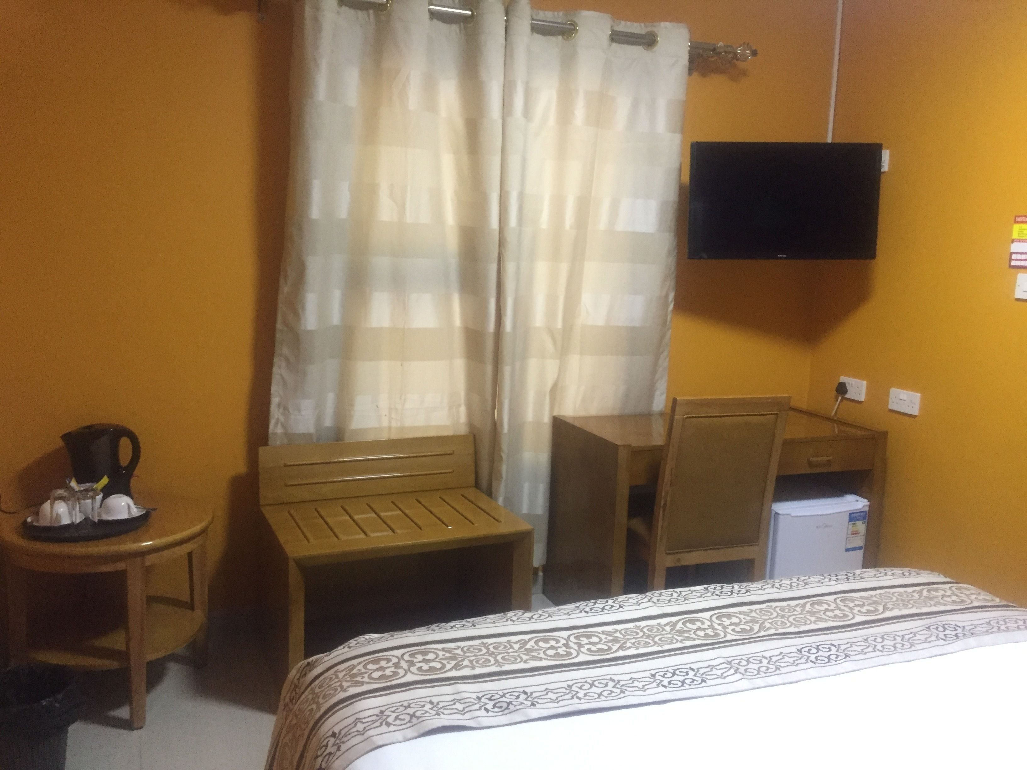 Une chambre d’hôtel équipée d’un lit, d’un bureau, d’une chaise, d’une petite table avec une cafetière et d’un téléviseur fixé au mur.