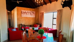 A cozy living room with a wooden dining table, red sofas, and a mounted bull head. - Zingela Nature Reserve - Leadwood Lodge (Blouberg)