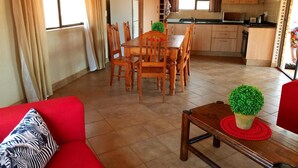 A compact living space with a dining area, kitchenette, and a red sofa with patterned cushions. - Zingela Nature Reserve - Leadwood Lodge (Blouberg)