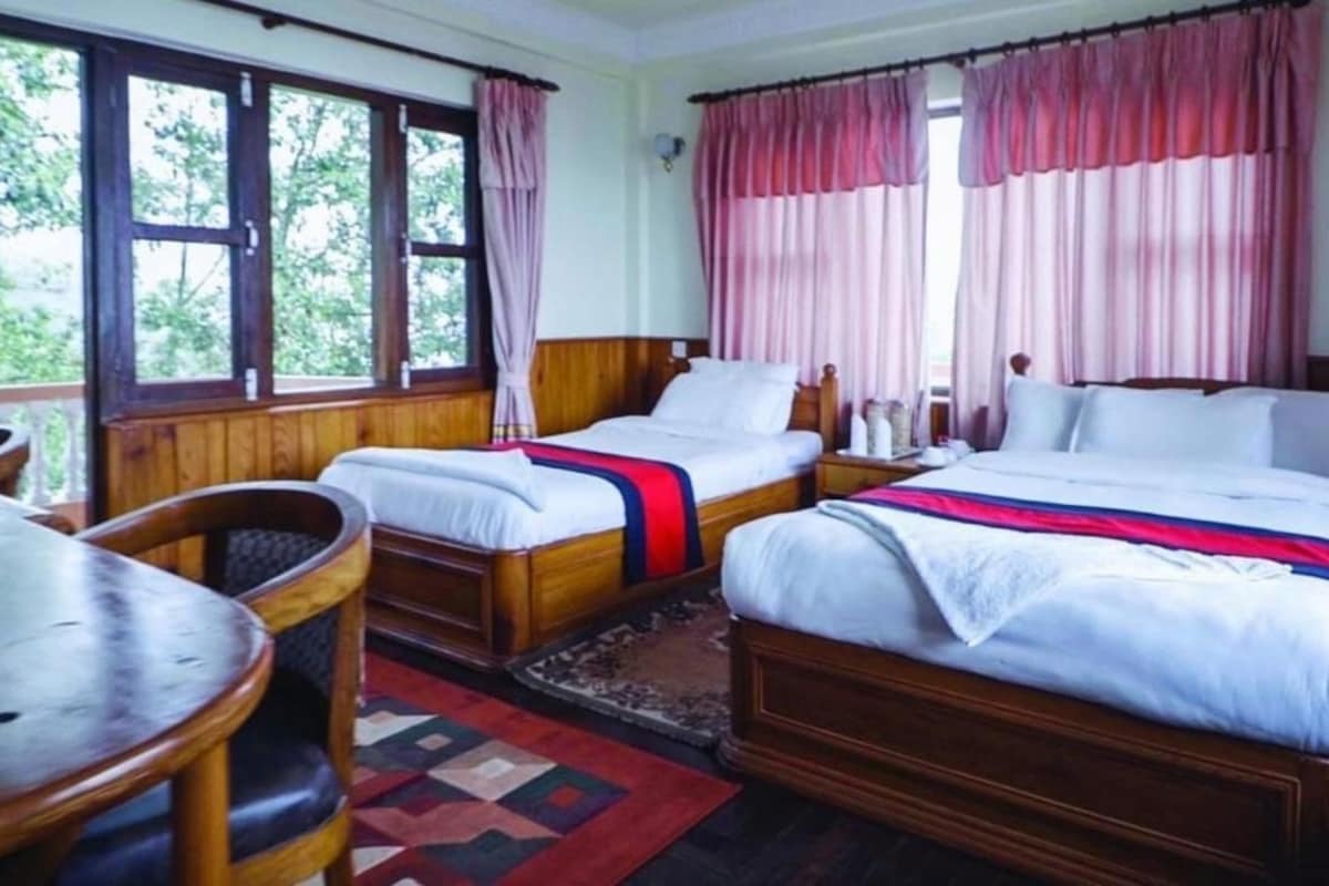 Een hotelkamer met twee houten bedden, een houten tafel en een raam met gordijnen.