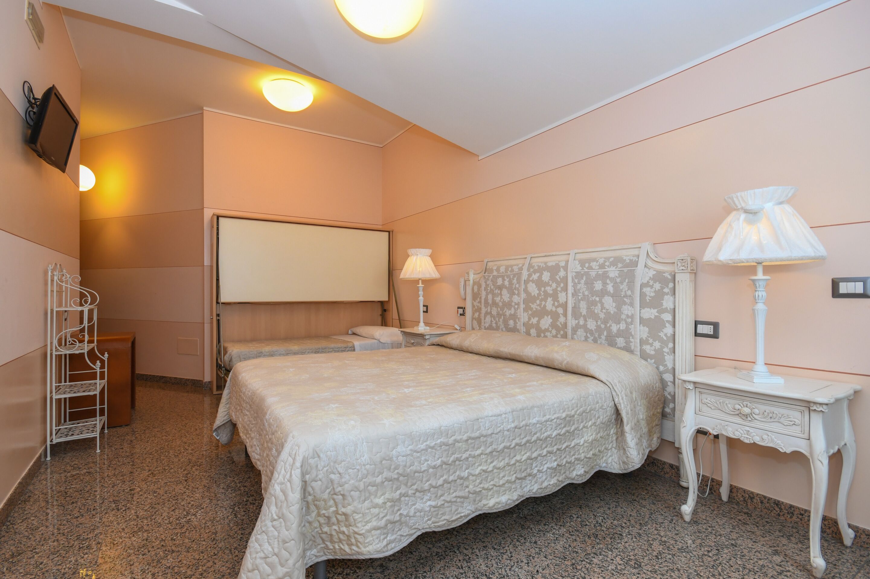 A hotel room with a large bed, a bedside table with a lamp, a TV mounted on the wall, and a small seating area with a chair and a side table.