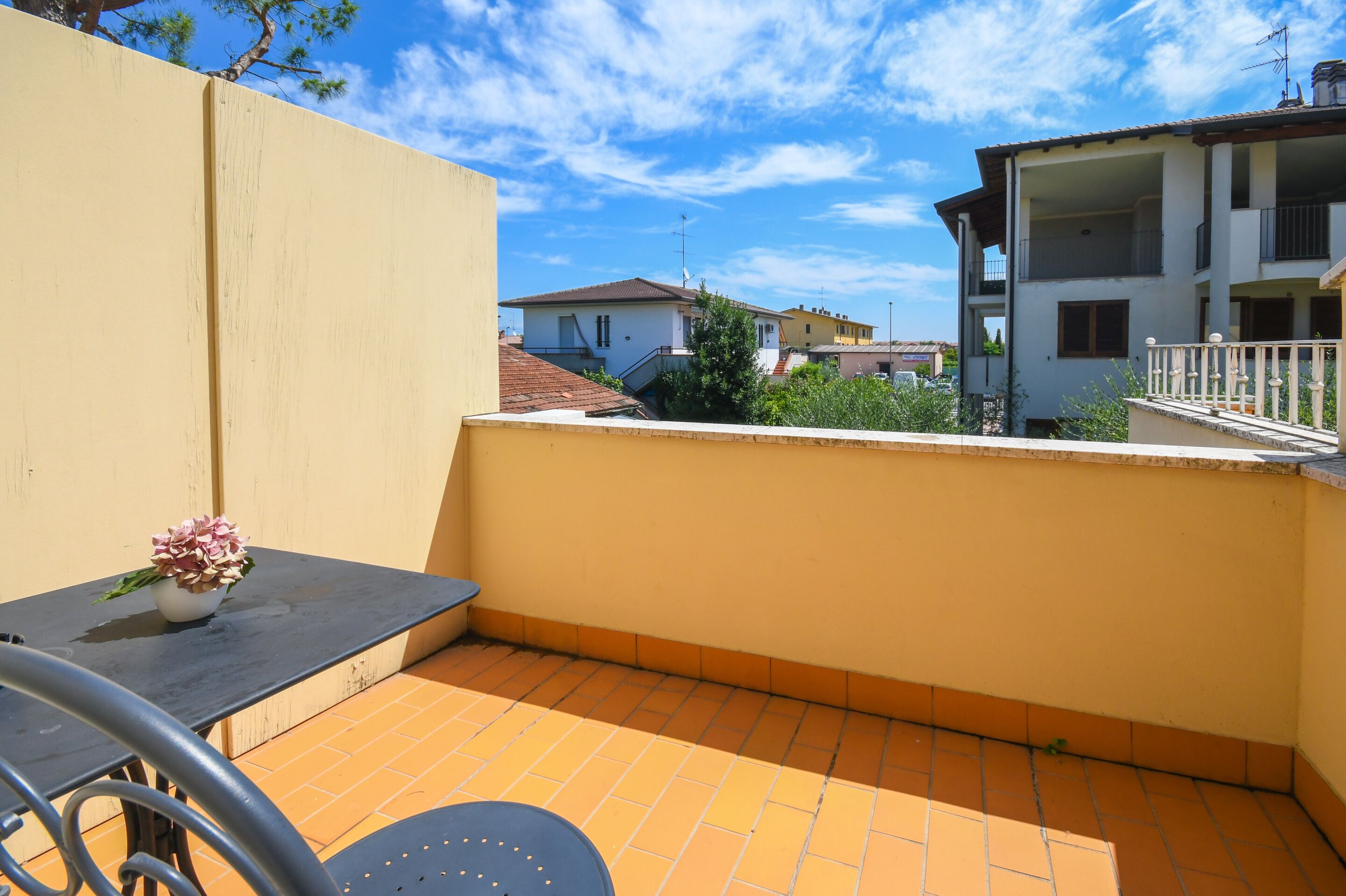 A small outdoor patio with a table and chairs, a potted plant, and a view of neighboring buildings.