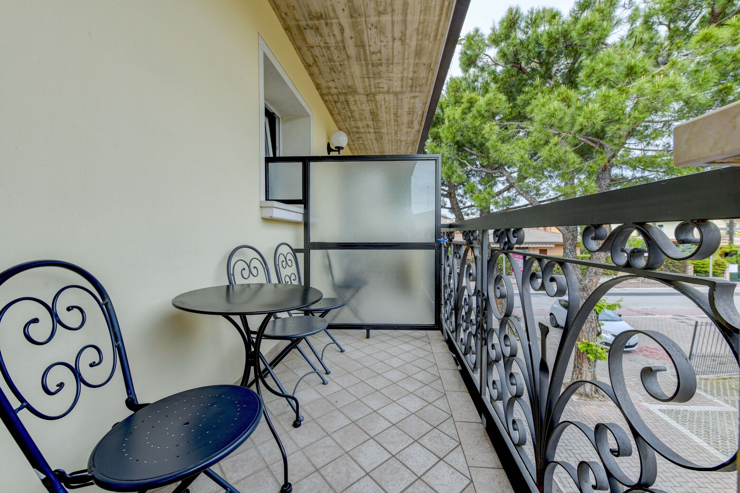 A balcony with a tiled floor, two metal chairs, a small round table, and a glass partition.
