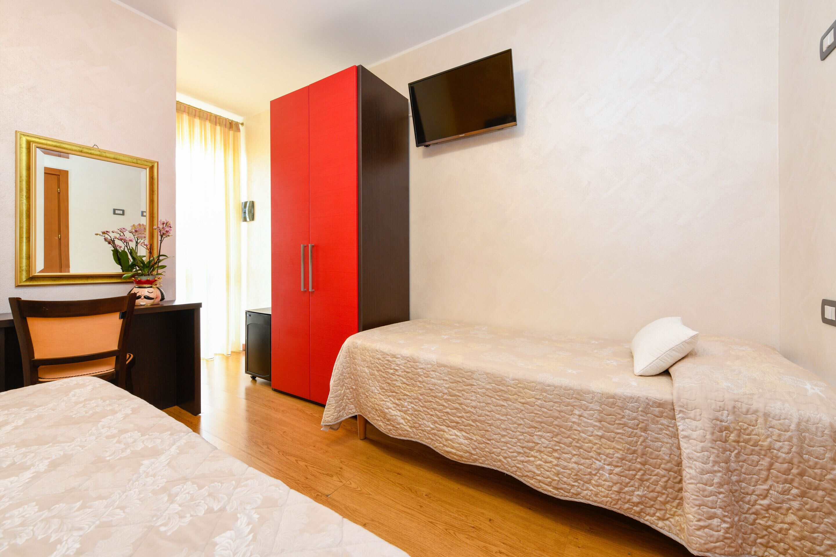 A hotel room with a bed, a desk, a chair, a wardrobe, and a TV.