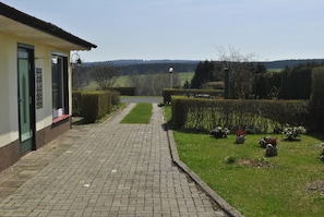 Un chemin pavé mène à un bâtiment doté d’une porte verte, entouré de haies bien entretenues et d’une pelouse.