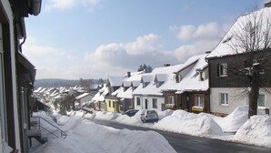 Une rue résidentielle bordée de maisons recouvertes de neige, une voiture garée le long de la rue et un ciel dégagé.