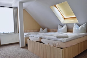 A bedroom with a sloped ceiling, a bed with white bedding, a window with curtains, and a radiator. - Pension Haus Mückenheim (Oberharz am Brocken)