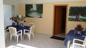 A dining area with a table set for two, white chairs, a vase with flowers, and a welcome mat. - Villa Iris (Thasos)