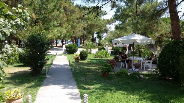A pathway leading through a garden with outdoor seating under umbrellas. - Villa Iris (Thasos)