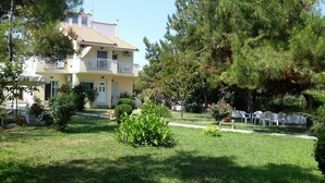 A two-story building with a balcony, surrounded by a well-maintained garden with various plants and a lawn. - Villa Iris (Thasos)