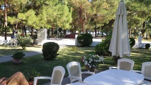 An outdoor seating area with white plastic chairs and tables, surrounded by greenery and trees. - Villa Iris (Thasos)