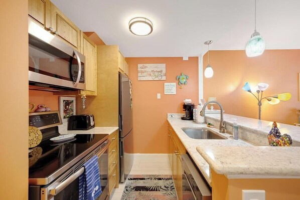 A kitchen with wooden cabinets, a microwave, a stove, and a sink. - ISLAND TIME at The Truman Annex in Key West (Key West)