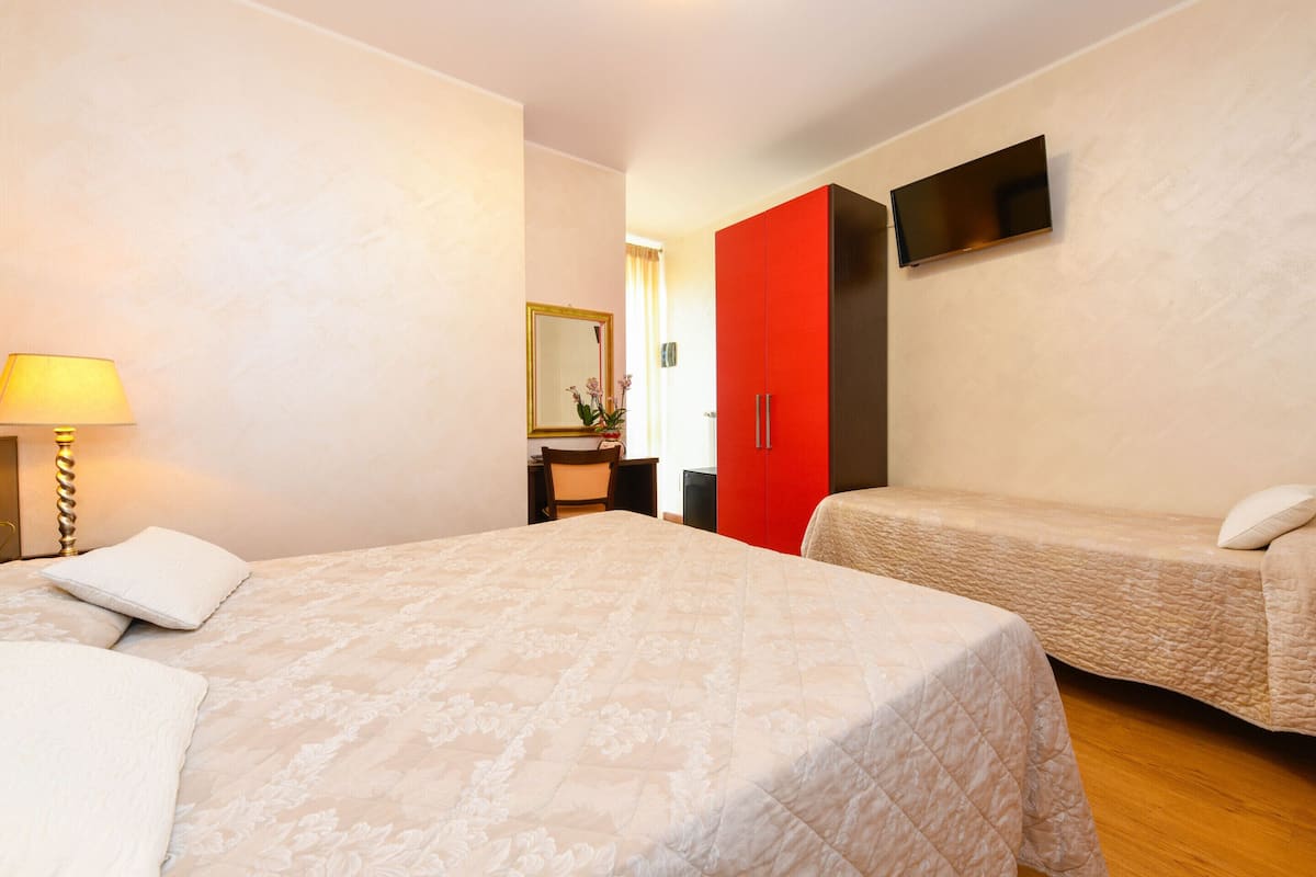Hotellihuone, jossa on kaksi sänkyä, seinälle asennettu televisio ja työpöytä tuolilla.