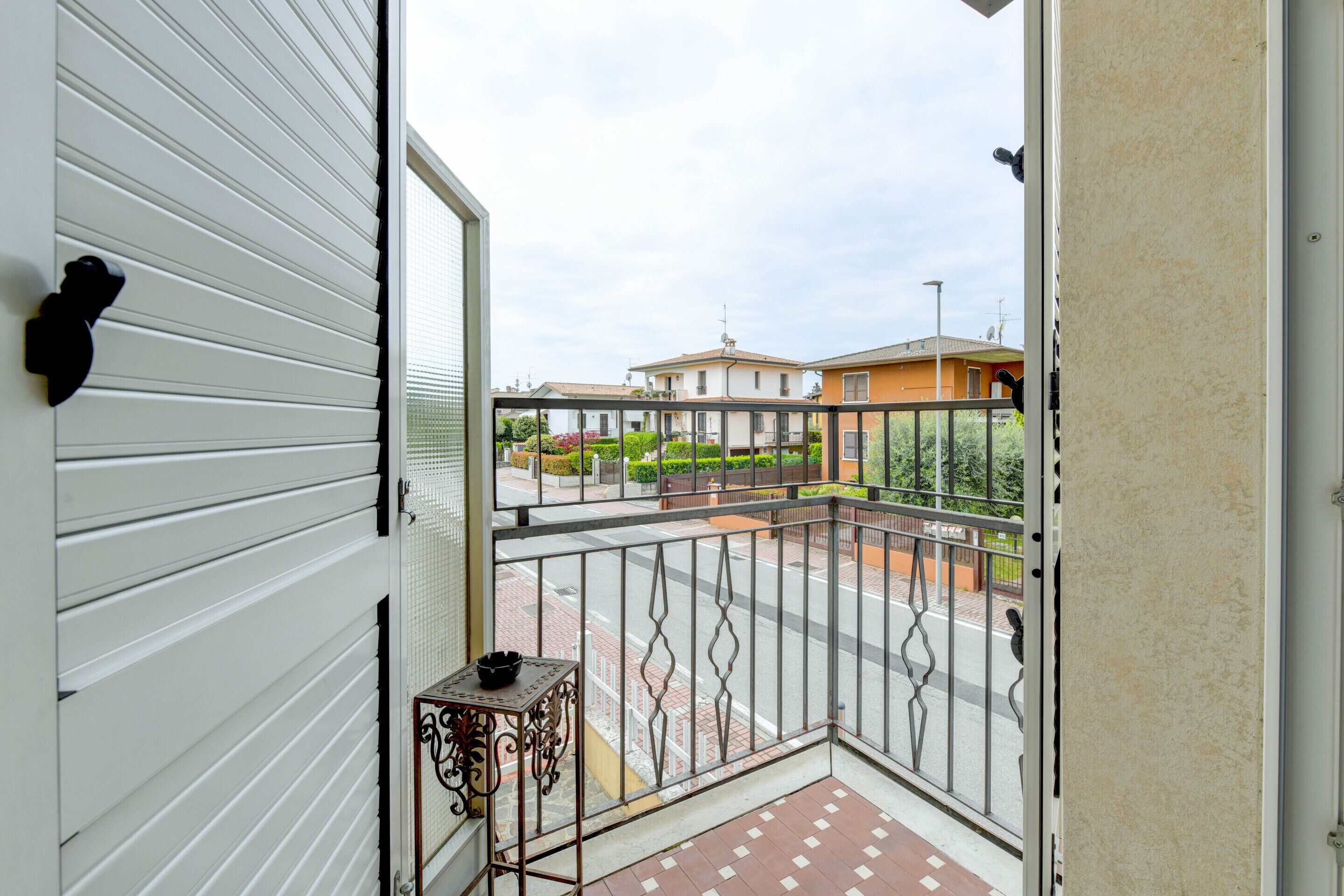 A balcony with a metal railing, a small table with a bowl, and a view of a street with houses.