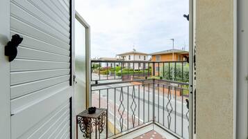 A balcony with a metal railing, a small table with a bowl, and a view of a street with houses.