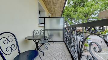 Een balkon met betegelde vloer, twee metalen stoelen, een kleine ronde tafel en een glazen scheiding.