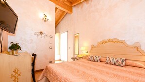 A bedroom with a wooden headboard, a bed with patterned bedding, a TV on a wooden dresser, and a potted plant. - B&B America (Sirmione)