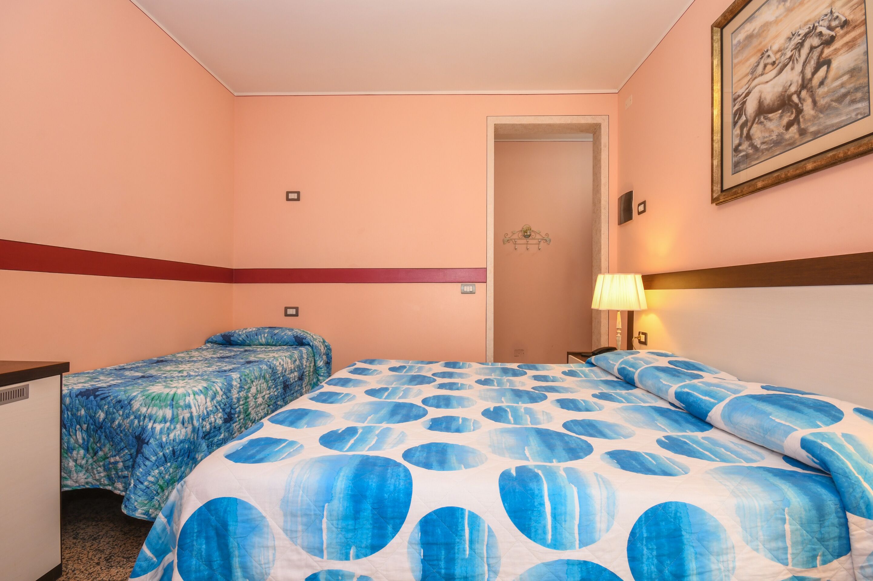 Habitación de hotel con dos camas, un escritorio, una lámpara y un cuadro en la pared.