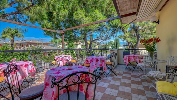 An outdoor patio with tables and chairs, surrounded by trees and a view of buildings in the background. - B&B America (Sirmione)