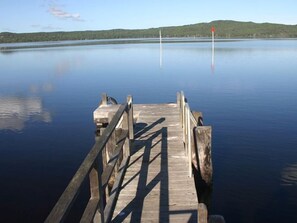 A wooden pier extending into calm water with a clear view of distant hills.