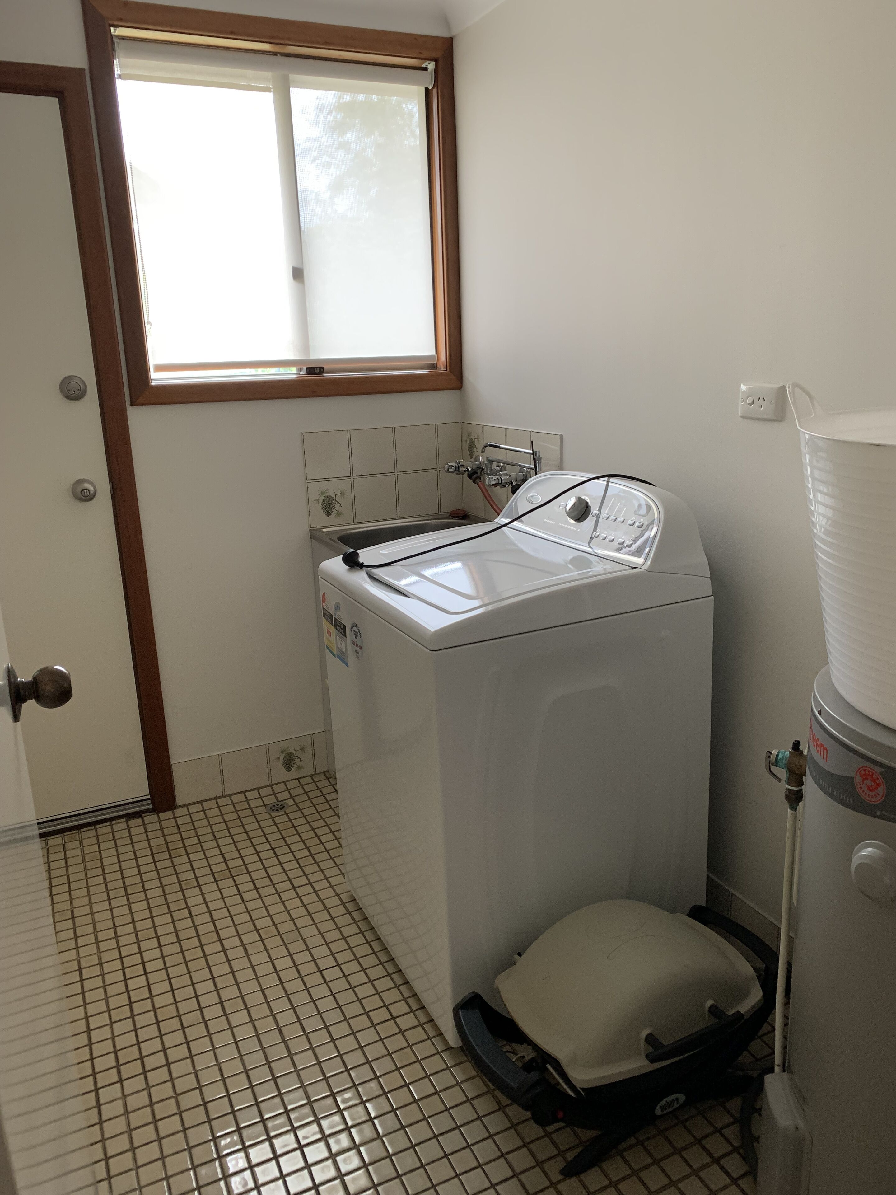 A compact laundry room with a front-loading washer and dryer, a window above the sink, and a tiled floor.