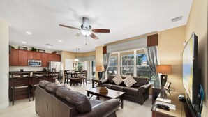 A modern living room with a sofa, coffee table, and TV. There is a dining area with chairs and a table, and a kitchen with cabinets and appliances. - Awesome! 6BR 4BA Luxury, Games, 2 Waterslides (Four Corners)