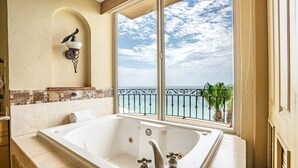A bathroom with a large bathtub, a window with a view of the sea, and a wall-mounted light fixture.