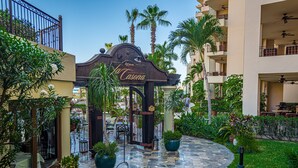 A courtyard with a restaurant entrance, palm trees, and outdoor seating.