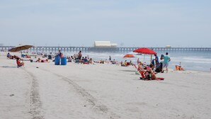 A beach with people relaxing under umbrellas, a pier in the background, and a large white building. - Great View w/o Oceanfront Prices-3BR 2.5BA -  (Myrtle Beach)