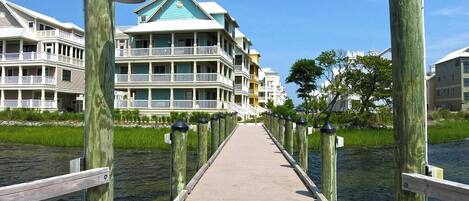 A wooden boardwalk leading to a waterfront property with multiple balconies and a green roof.
