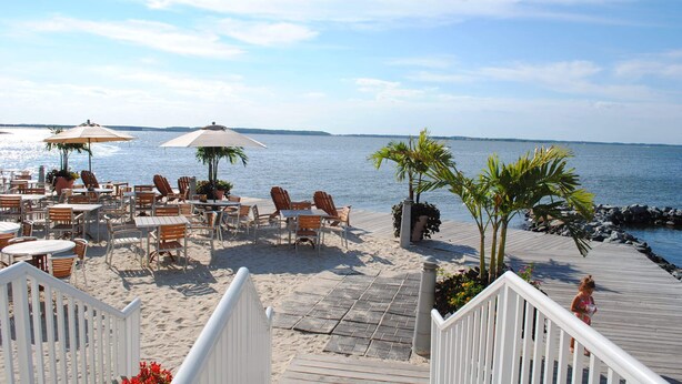 A beachside patio with outdoor seating and umbrellas overlooking the sea. - Bright, fun 5-bedroom townhouse in exclusive gated community with free WiFi, an indoor/outdoor pool, private bayside beaches, a restaurant, and more! (Ocean City)