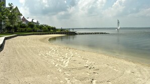 A sandy beach with footprints, a sailboat, and houses in the background. - Bright, fun 5-bedroom townhouse in exclusive gated community with free WiFi, an indoor/outdoor pool, private bayside beaches, a restaurant, and more! (Ocean City)