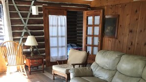 L’intérieur d’une cabane en rondins, avec un canapé en cuir, un fauteuil à bascule en bois et une petite table.