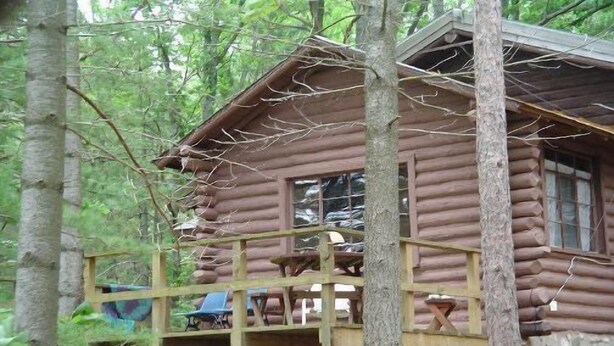 Une cabane rustique en rondins de bois, dotée d’une terrasse en bois et d’un petit porche.