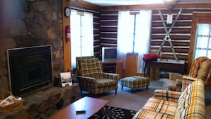 L'intérieur d'une cabane en rondins, avec une cheminée, des meubles à motifs écossais et un téléviseur.
