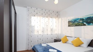 Un dormitorio con cama, un cuadro y una ventana con cortinas traslúcidas.