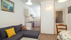 Un espacio habitable compacto con sofá, mesa de comedor, kitchenette y una puerta que conduce a otra habitación.