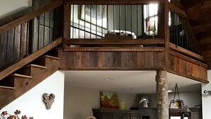 A spacious living area with a high ceiling, a wooden staircase leading to an upper level, a kitchen with modern appliances, and a cozy seating area with a sofa and decorative wall art. - Unique -Oliver Creek Cabin in Wilderness-PRIVATE-King Bed, WiFi, Hot Tub, Hiking (Ellijay)