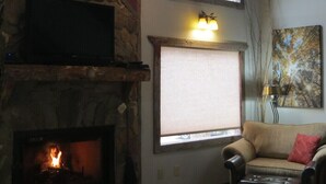 A cozy living room with a stone fireplace, a large window, a sofa, and a painting on the wall. - Unique -Oliver Creek Cabin in Wilderness-PRIVATE-King Bed, WiFi, Hot Tub, Hiking (Ellijay)