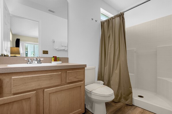 Un baño moderno con tocador de madera, inodoro blanco y zona de ducha.